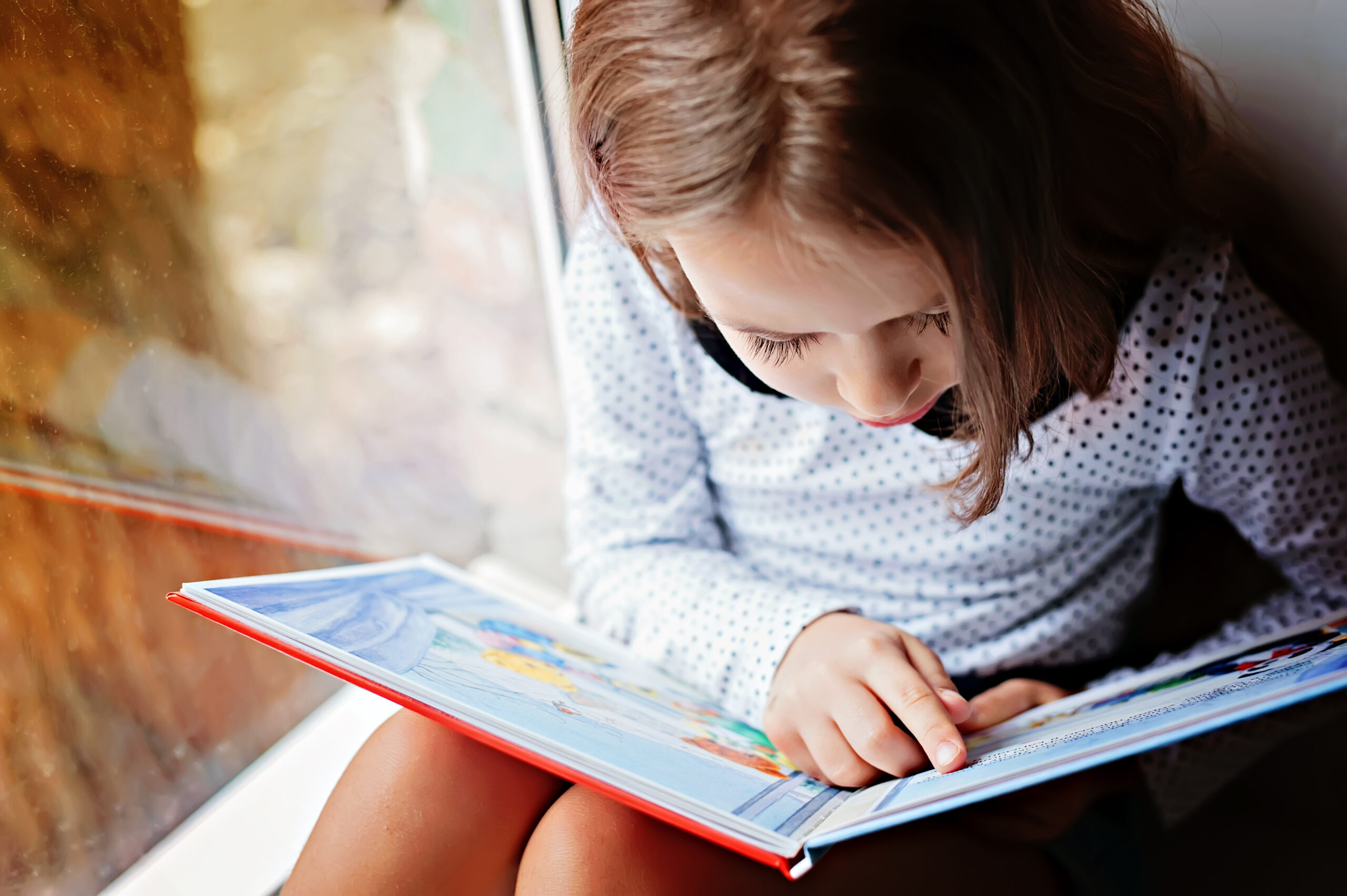 elementary aged girl reading a book near the window